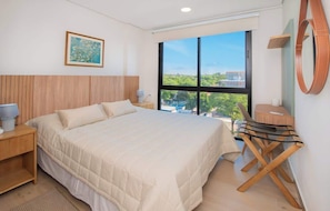 Quarto de hotel com uma cama grande, uma escrivaninha, uma cadeira, uma janela com vista e um quadro na parede.