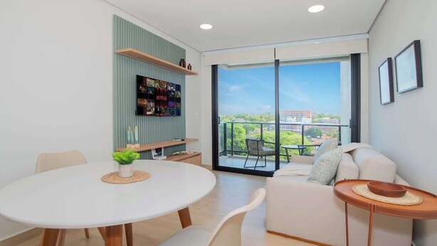 Ein modernes Wohnzimmer mit einem runden Esstisch, weißen Sofas und einem Balkon mit Blick.