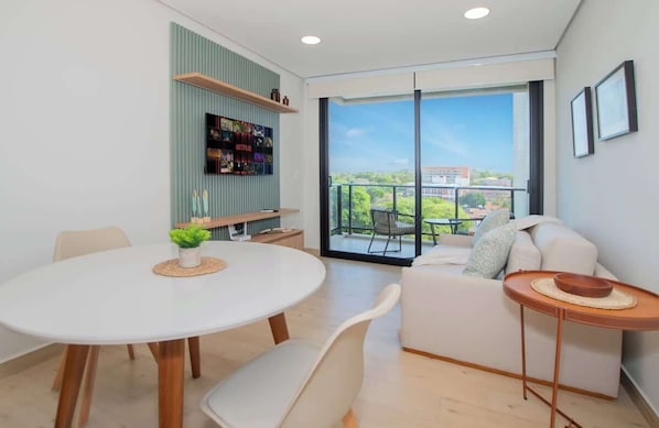 Sala de estar moderna com mesa de jantar redonda, sofás brancos e varanda com vista.