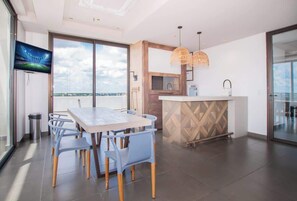 Eine moderne Küche mit einer großen Kochinsel, einem Essbereich mit Tisch und Stühlen sowie Blick durch große Fenster.