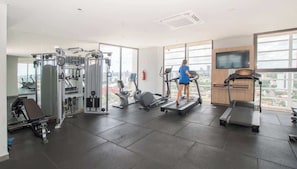 Ein Fitnessstudio mit Cardiogeräten, Krafttrainingsgeräten und einem Fernsehbildschirm.