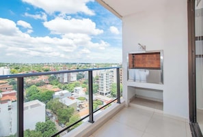 Ein Balkon mit Blick auf eine Stadtlandschaft, einem Metallgeländer und einem kleinen, umzäunten Bereich mit einem Metallgitter.