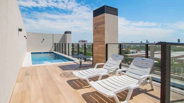A rooftop pool area with two lounge chairs, a table, and a view of the cityscape.