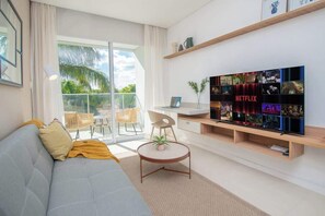 A modern living room with a sofa, a round coffee table, a TV on a wooden shelf, and a balcony with outdoor furniture. - In the heart of Villamorra, Rooftop Pool & BBQ (Asunción)