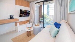 Un soggiorno moderno con divano, televisione a parete, un piccolo tavolo rotondo e un balcone con posti a sedere esterni.