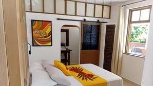 A hotel room with a bed, a window, a door, and a painting on the wall. - Aremiti - Fare Orotia (Avera, Raiatea)