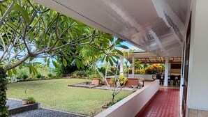 A covered outdoor area with a red patterned floor, a grassy lawn, and potted plants. - Aremiti - Fare Orotia (Avera, Raiatea)