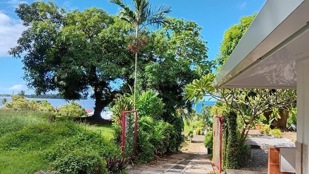 A pathway leading to a building with a view of a lake and lush greenery. - Aremiti - Fare Orotia (Avera, Raiatea)