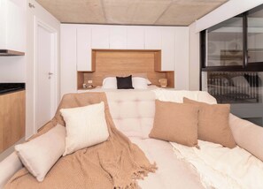 Quarto com cama, almofadas, mesa de cabeceira e janela.