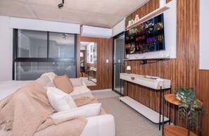 Quarto de hotel moderno com uma cama grande, televisão fixada na parede e pain éis de madeira.