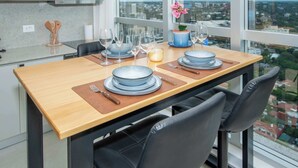 Una mesa de comedor dispuesta con platos, vasos y cubiertos, con vistas a la ciudad a través de amplias ventanas.