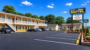 Un motel composé d’un bâtiment à deux étages, d’un parking et d’un panneau publicitaire indiquant des tarifs hebdomadaires avantageux, la présence d’un mini-réfrigérateur et d’une connexion Wi-Fi gratuite.