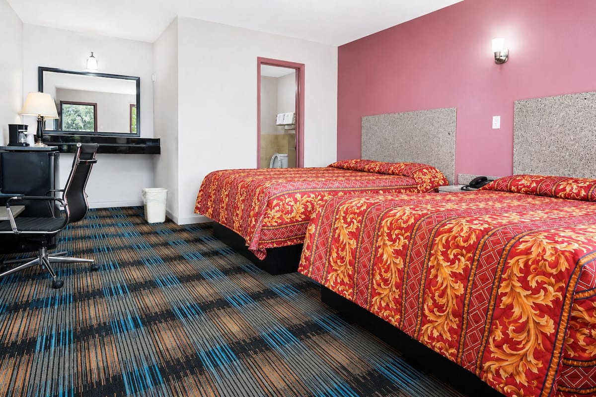 A hotel room with two beds, a desk, a chair, a mirror, and a door.