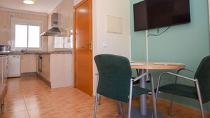 A compact kitchen with a microwave, stove, and sink, a dining area with two chairs and a table, and a TV mounted on the wall. - Ref: 258. Charming attic apartment in Los Boliches close to the beach (Fuengirola)