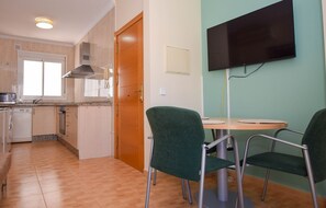 Eine kompakte Küche mit Mikrowelle, Herd und Spüle, ein Essbereich mit zwei Stühlen und einem Tisch sowie ein an der Wand befestigter Fernseher.