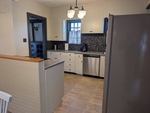 A kitchen with a dishwasher, a refrigerator, and a window with curtains. - Home in 4th & Gill Near Downtown (Knoxville)
