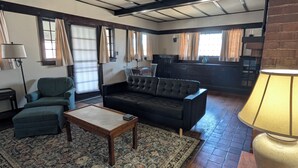 Een woonkamer met een bank, fauteuil en salontafel, een kamerbreed tapijt met patroon en een open haard.