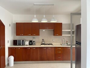 A modern kitchen with wooden cabinets, a microwave, a stove, and pendant lighting. - Casa Bahia Private Azul, Nayarit (Mezcales)
