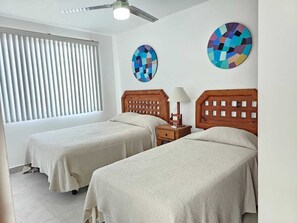 A room with two beds, a ceiling fan, a window with blinds, and two wall art pieces. - Casa Bahia Private Azul, Nayarit (Mezcales)