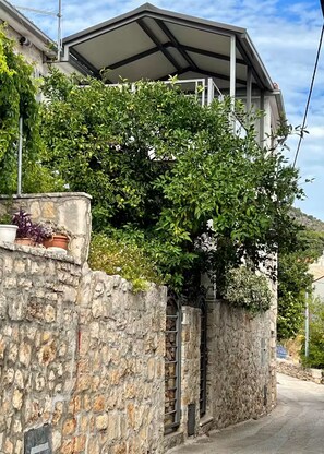 Eine Steinmauer mit einem Metallgitter, einem überdachten Balkon und üppiger Bepflanzung.