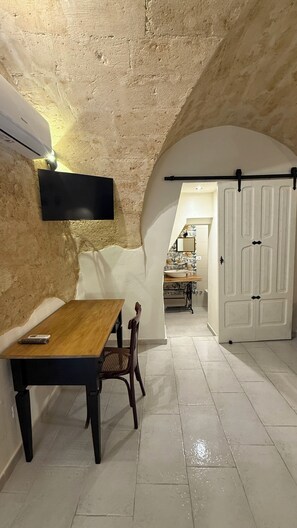 Une pièce avec une table en bois, une chaise, un climatiseur fixé au mur et une porte dotée d’une poignée noire.