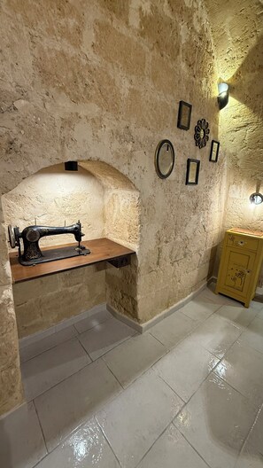Une pièce comprenant une machine à coudre ancienne posée sur une étagère en bois, un miroir fixé au mur et un petit meuble avec un panneau d’affichage en liège.