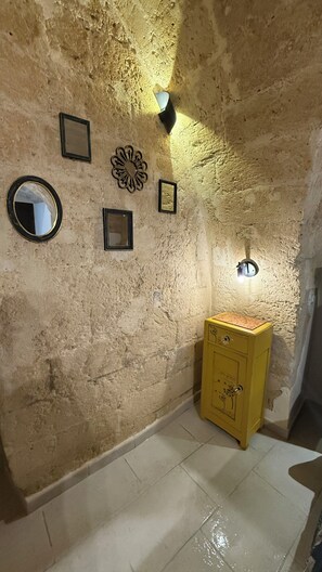 Une pièce aux murs à la texture rugueuse, avec un meuble jaune et plusieurs objets encadrés accrochés au mur.