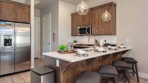 Eine moderne Küche mit Holzschränken, Edelstahlgeräten, einer zentralen Kochinsel mit Hockern und Pendelleuchten.