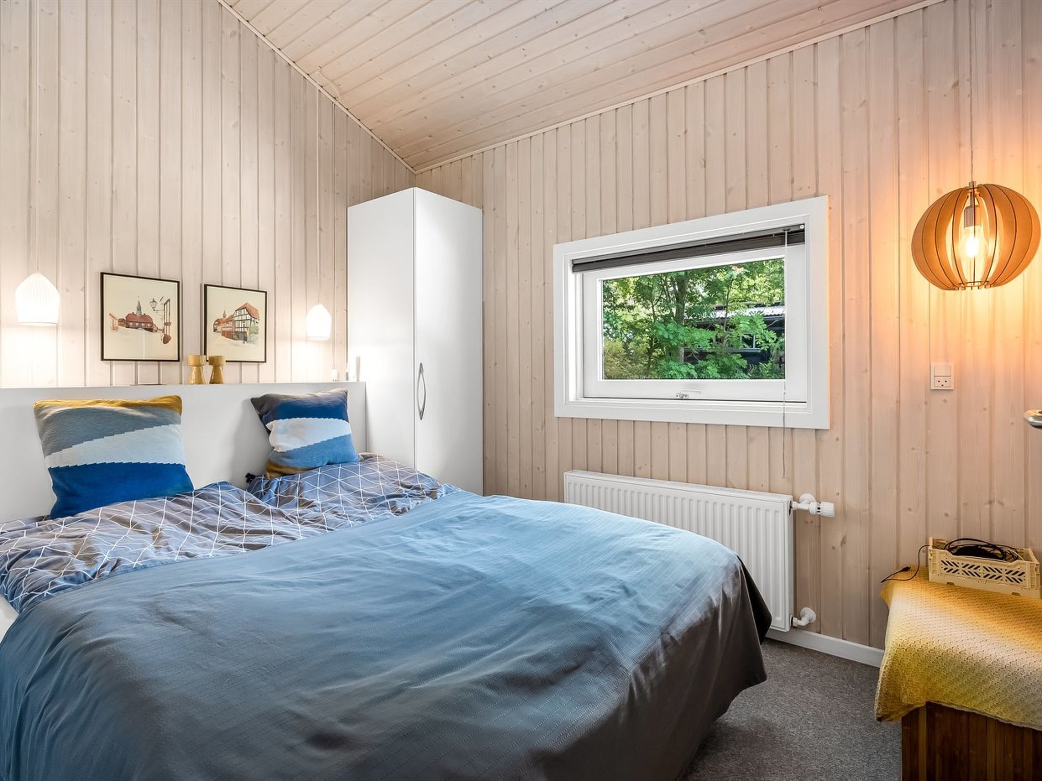 Ein Schlafzimmer mit Bett, Fenster, Heizkörper und Wandleuchten.