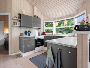 Eine moderne Küche mit grauen Schränken, einem eingebauten Backofen, einer Arbeitsplatte aus Granit und einem Fenster mit Blick auf Grünflächen.