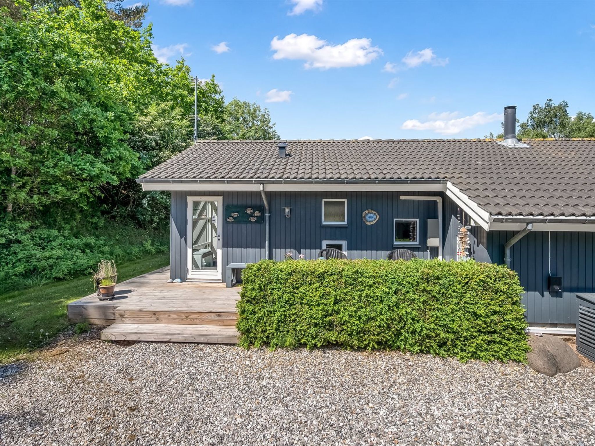 Et hus med tegltag, en fordør og en lille veranda med stole.