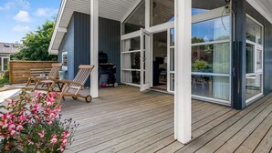Una casa moderna con una terrazza in legno, ampie vetrate e un patio coperto.