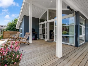 Ein modernes Haus mit einer Holzterrasse, großen Glasfenstern und einer überdachten Veranda.