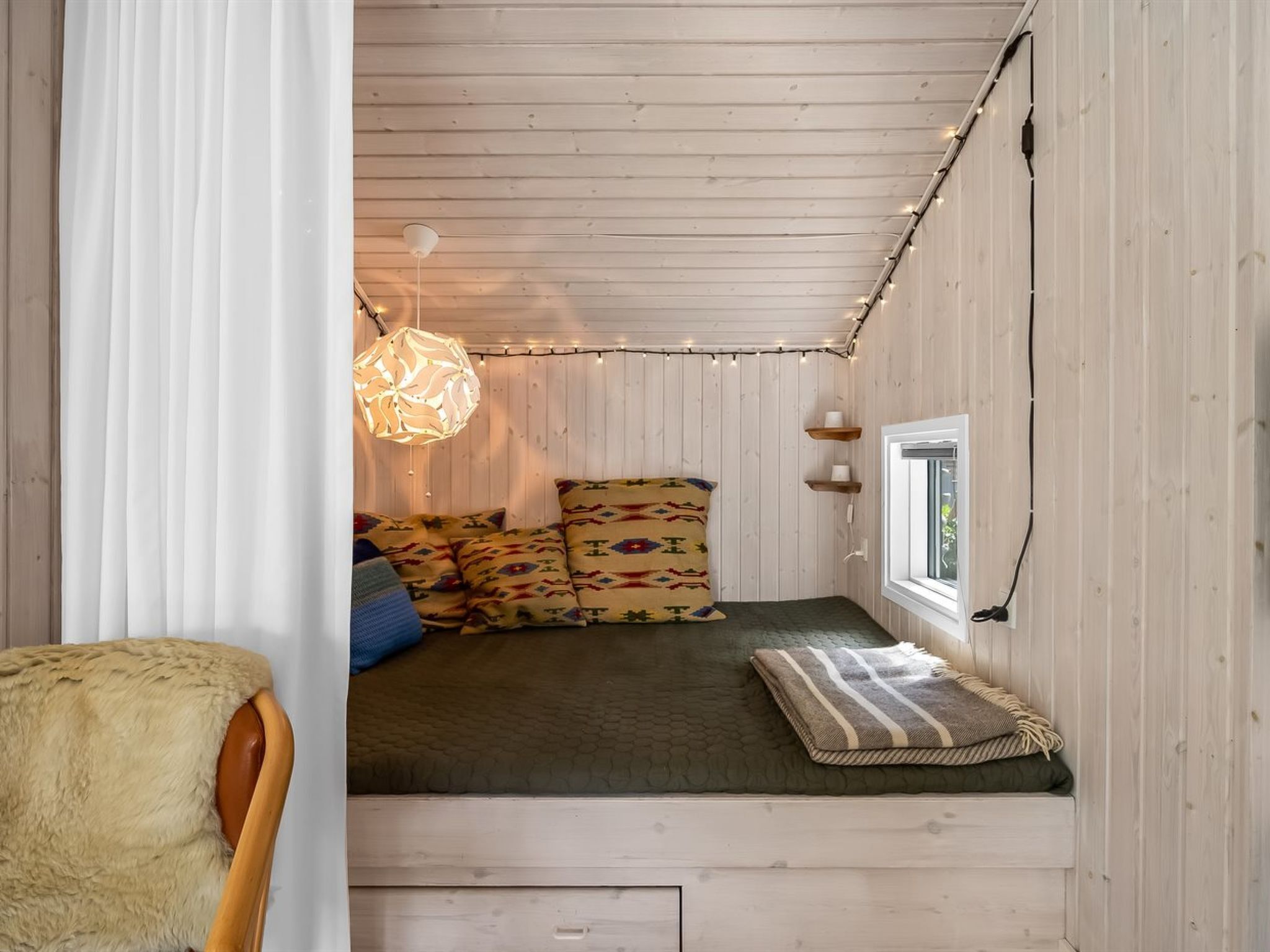 Une chambre confortable, aménagée dans le style d’un chalet, avec un lit, des oreillers, un luminaire suspendu et une fenêtre.