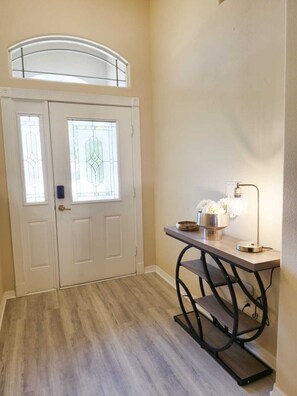 A hallway with a white door with glass panels, a small table with a lamp, and a bench.