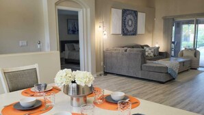 A dining area with a table set for four, a chandelier, and a sofa in the background.