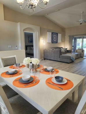 A dining area with a table set for four, a chandelier, and a sofa in the background.