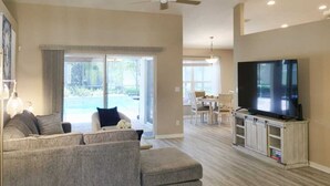 A spacious living room with a large sofa, a flat-screen TV, and a dining area with a table and chairs.