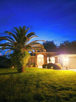 A residential house with a well-maintained lawn, a palm tree, and a garage.