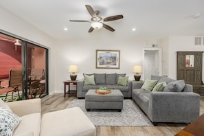 A living room with a grey sofa set, a coffee table, a ceiling fan, and a painting on the wall. - CASA CHOLLA - Updated unit with sunrise & pool views. (Phoenix)