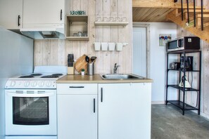 A kitchen with a stove, sink, and wooden wall paneling. - Cozy Lakeside Cabin Retreat with Beach, Kayaks, Fire Pit & Trails (Sainte-Marguerite-du-Lac-Masson)
