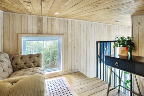 A wooden-paneled room with a sofa, a small table, and a window with a view of trees. - Cozy Lakeside Cabin Retreat with Beach, Kayaks, Fire Pit & Trails (Sainte-Marguerite-du-Lac-Masson)