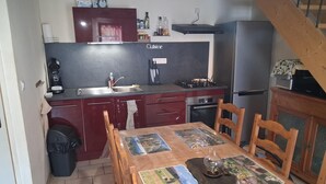 Et lille køkken med et spisebord til fire personer, en komfur og et køleskab.