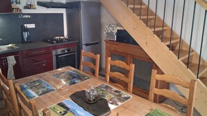 Et kompakt køkken med gasblus, ovn og køleskab. Et træspisebord med stole er placeret under en trappe.