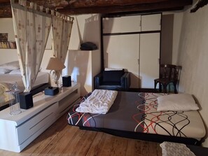 Une chambre à coucher comprenant un lit, une table de chevet, une lampe, une chaise, une armoire et une fenêtre avec des rideaux.