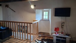 Et værelse med en trætrappe, et fjernsyn ophængt på væggen, et lille bord med en rød lampe og en kohudstæppe.