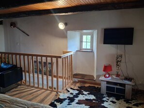 Ein Zimmer mit einer Holztreppe, einem an der Wand befestigten Fernseher, einem kleinen Tisch mit roter Lampe und einem Kuhfellteppich.