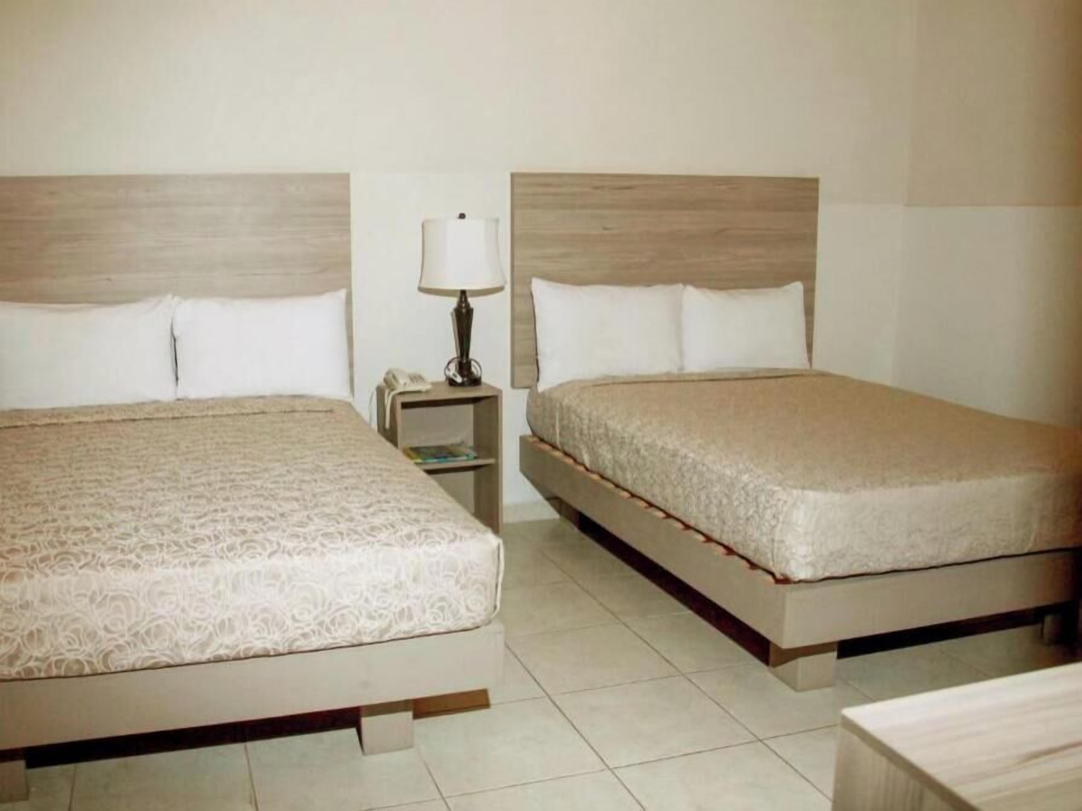 Two beds with headboards, a bedside table with a lamp, and a nightstand with a phone.