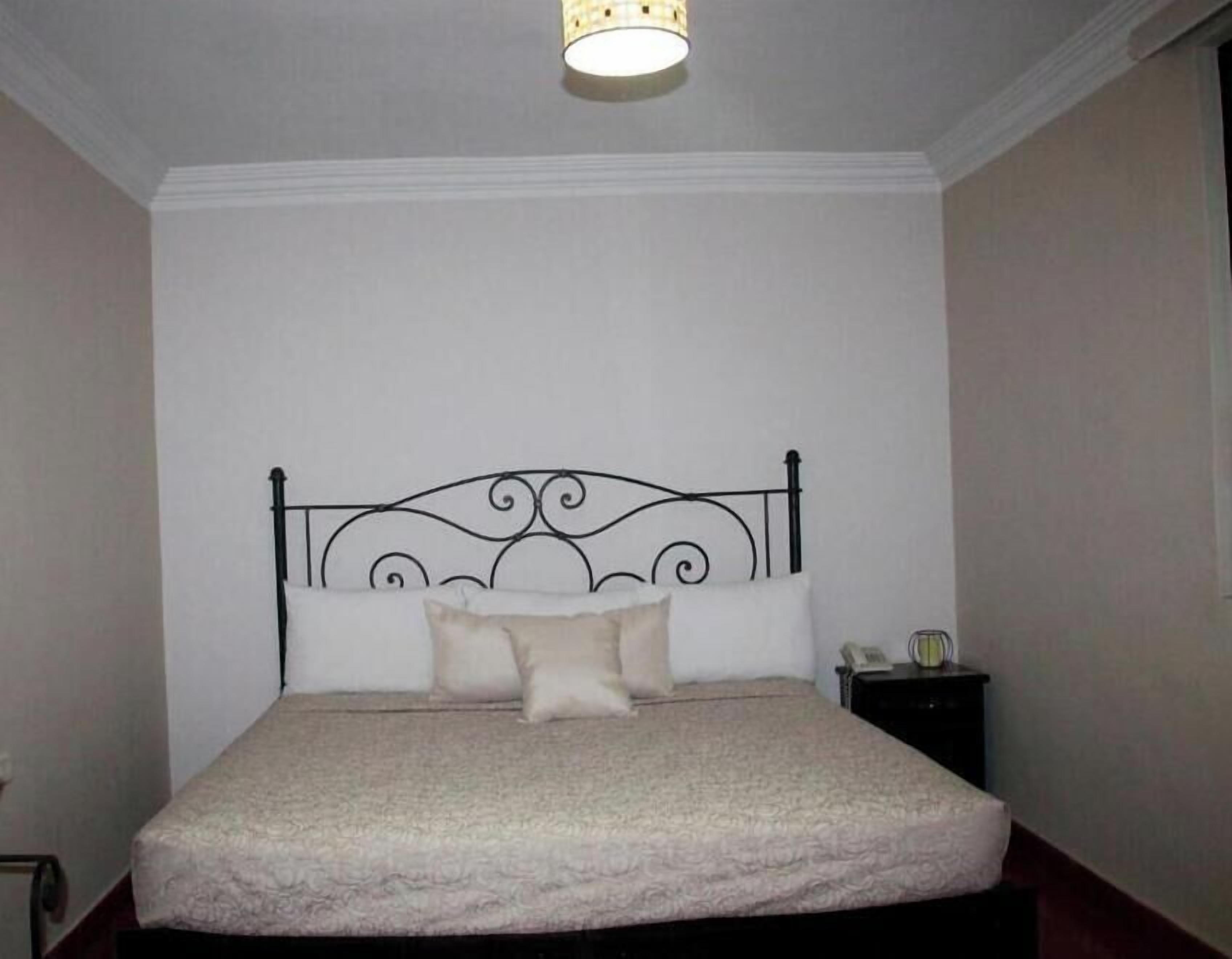 Un lit simple avec une tête de lit en métal, une table de chevet avec une lampe et un mur uni.