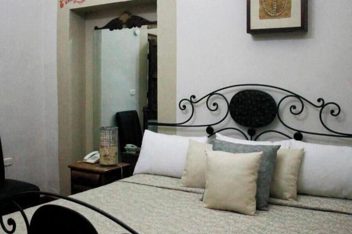 A bedroom with a bed, pillows, a nightstand, a phone, and a mirror.